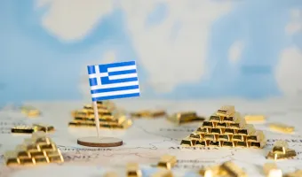 A small Greek flag positioned on a world map, surrounded by scattered gold ingots