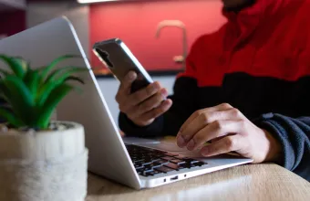 Man typing on a laptop and holding a smartphone