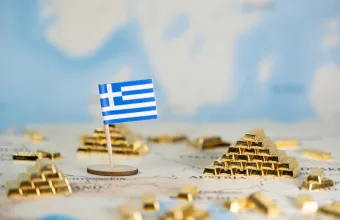 A small Greek flag positioned on a world map, surrounded by scattered gold ingots